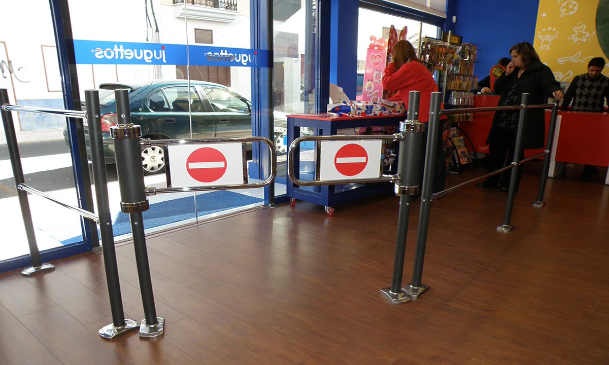 Entrada de un comercio con banderolas metálicas y valla de limitación antes de la línea de cajas