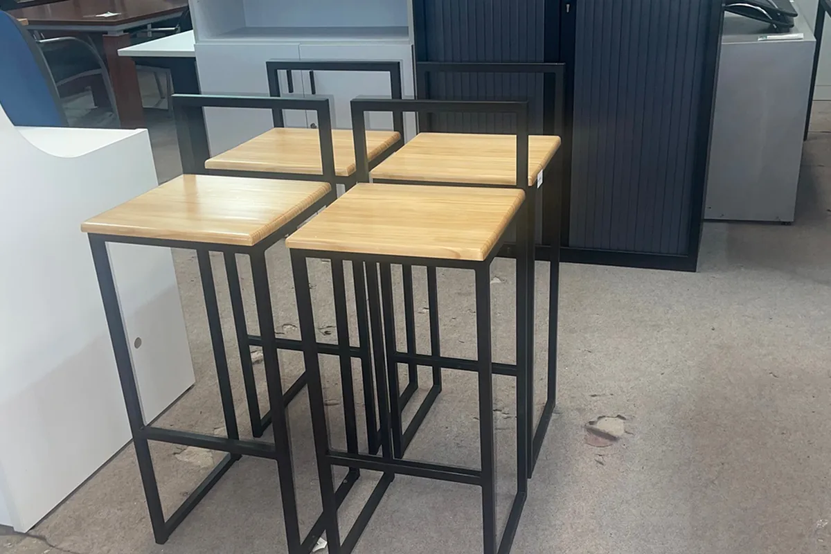 Cuatro taburetes altos fijos de madera y hierro negro, con travesaño para los pies, en la nave de Muebles Talego